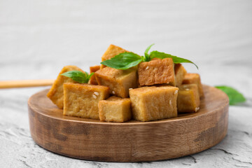 Wooden plate with delicious fried tofu, basil and sesame seeds on light grey table