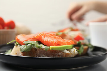 Tasty bruschetta with salmon, arugula and avocado on black plate, closeup