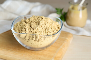 Bowl of aromatic mustard powder on wooden table, closeup