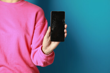 Woman showing damaged smartphone on light blue background, closeup. Device repairing