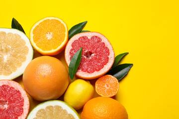 Different ripe citrus fruits with green leaves on yellow background, flat lay. Space for text