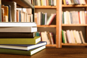 Many stacked hardcover books on wooden table in library, space for text