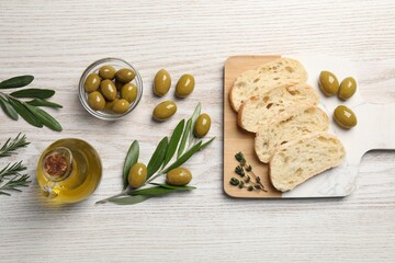 Cooking oil in jug, olives, herbs and ciabatta bread on wooden table, flat lay