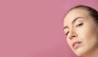 Fototapeta premium Girl's face with water drops on her face looks at the camera Relaxation Close up Horizontal frame Purple background Beauty ,Cosmeics,Fashion Horizontal frame Space for text on the left