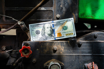Hundred dollar bill on a tractor engine close-up. Money and the agricultural industry stopped. Payment for the services of a tractor driver - obrazy, fototapety, plakaty