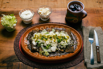 Enfrijoladas served in a clay dish. Typical Mexican food. Bean tacos with cream and cheese.