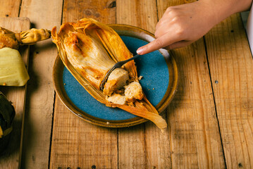 Hands of a person cutting a tamale with a fork. Tamale, typical Mexican food.