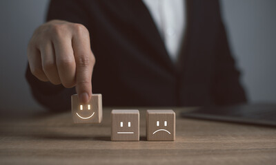 Close up customer hand choose smiley face and blurred sad face icon on wood cube, Service rating, satisfaction concept.