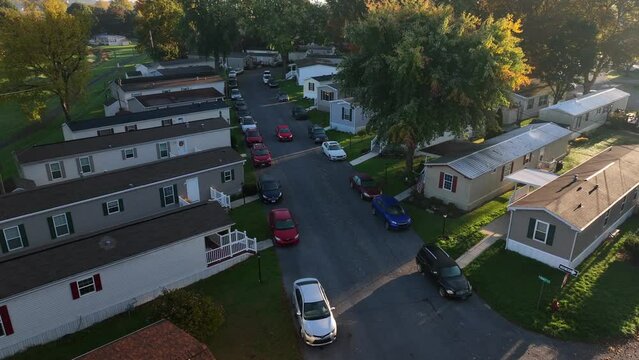 Cars tightly parked in mobile home trailer park. Low income housing in USA during autumn fall season. Aerial view as car drives on street.