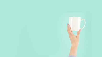 Arms raised up holding tea cup on green background.