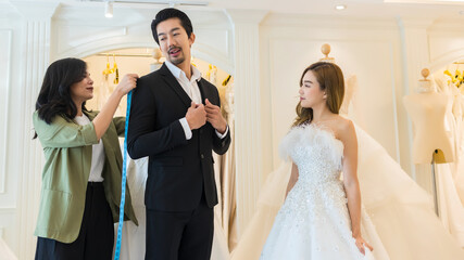 Naklejka premium Bride and groom wear dress and try to fitting in modern wedding studio with bridal store owner 
