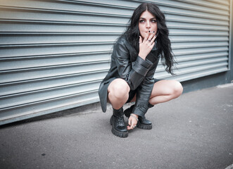 Punk, emo and woman smoking a cigarette in the street of an urban city in Canada in an edgy black outfit. Grunge, rocker and girl smoker with tobacco to smoke while sitting in the road in town. - obrazy, fototapety, plakaty