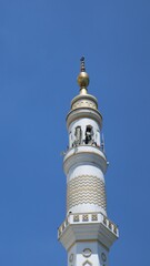 Fototapeta na wymiar Low angle view Single Minaret of Muslim mosque on the clear blue sky background. Islam, religion and architecture, and travel concept. Mosque design in Islamic religious architectural traditions.