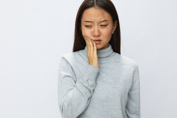 Asian woman holding her hand to her jaw in severe dental pain, white background