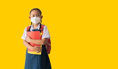 Asian school girl in uniform wear medical face mask, With backpack and holding book isolate on yellow background