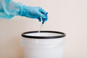 Doctor throwing used syringe into trash can, close-up of hand in protective medical glove