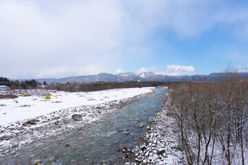 蓮華大橋（長野県）から撮影した、雪が積もった河原と川と壮大な山の風景写真