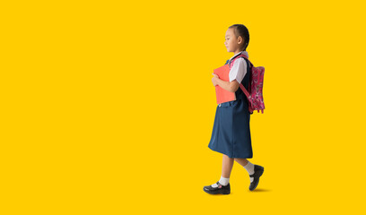 Fototapeta premium Asian student child girl wears school uniform holding book with walking back to school, isolated on yellow background
