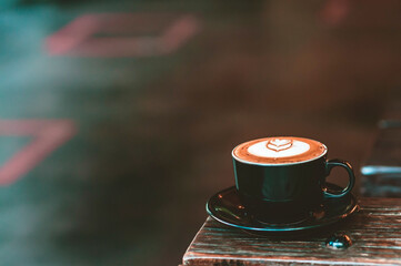 Hot latte coffee in black cup placed on vintage wooden table