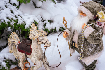 Toy Santa Claus with a wooden rocking horse in the snow under the Christmas tree