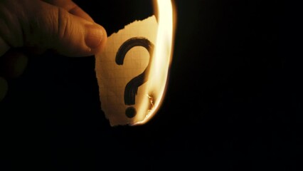 A man burns paper with a question mark in the dark. - Powered by Adobe