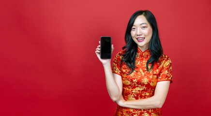 Asian chinese woman with red cheongsam or qipao holding mobile phone for Chinese New Year celebration holiday isolated on red background concept