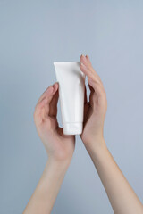 Woman's hands holding a tube of white cream. Cosmetics mockup.