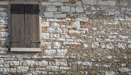 Background with a wall of different bricks and a window with closed wooden shutters