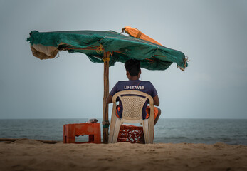 Lifesaver Lifeguard sitting on a chair on the  beach under the umbrella near the ocean backshot