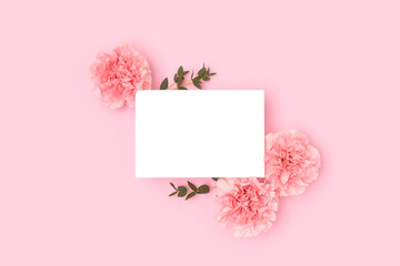 Clean paper card mock up, carnation flowers and green eucalyptus branches on a pink background. Greeting card concept.