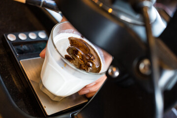 Close-up of stream of coffee flowing from an espresso machine into a transparent cup, poured directly onto cold milk, Dirty coffee