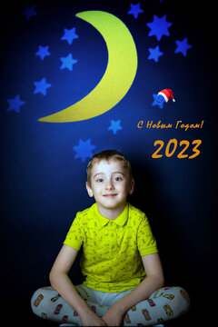 A cute boy child sits in a children's room with an interior against the background of the stars and the moon with the effect of oil paint. Postcard: Happy New Year.