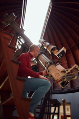 Astronomer with a big astronomical telescope in observatory doing science research of space and...