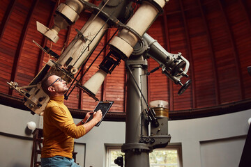 Astronomer with a big astronomical telescope in observatory doing science research. - obrazy, fototapety, plakaty