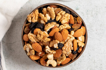Raw mixed nuts on gray background. Walnuts, almonds, hazelnuts and raisins in a coconut bowl. Top view