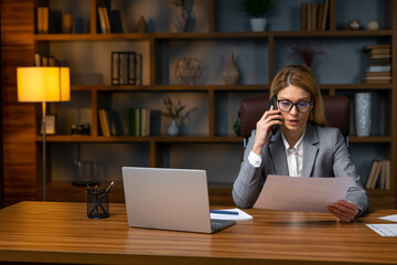 Serious business woman talking on smartphone and reading document, solving corporate business problem. Female employee discussing document by cellphone, receive news.