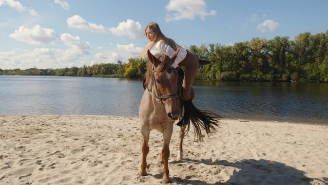 Calm, tranquil weekend at equestrian club with picturesque, fall nature around. Woman riding a horseback along sandy river shore. High quality 4k footage