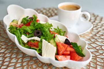 greek salad in a wavy plate with a cup of coffee