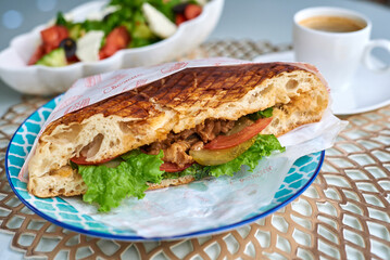 Shawarma in a flatbread. With a mug of coffee, salad in the background