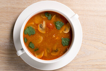 Mushroom soup with greens in a white bowl on a wooden background