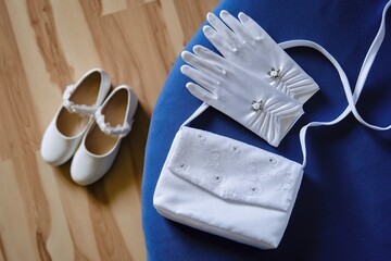 torebka i rękawiczki komunijne białe na stole z bucikami w tle