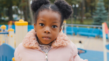 Close up serious child face portrait cute little African American kid sad upset close-up alone small girl baby daughter looking at camera calm ethnic child after school standing at playground outdoors