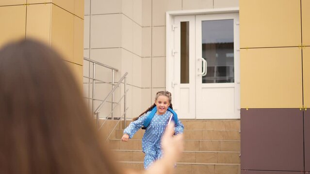 Happy girl run from school to her mother. Children education. Girl with backpack and book runs from school. Happy children and parents in the school park. Family education. Mother's Day in childcare.
