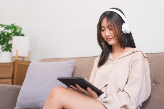 Concept of relaxation at home, Young Asian woman listening music and surfing social media on tablet