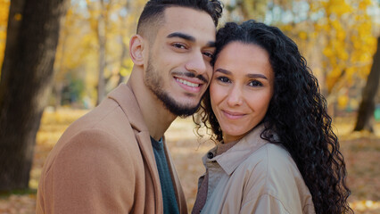 Fototapeta premium Close-up portrait outdoors Hispanic ethnic multiracial couple in love in autumn park looking at camera guy man and girl woman smiling stand close to each other touching heads lovers on romantic date
