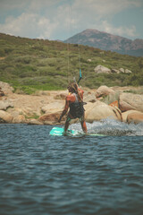 Woman kite-surfing standing on her kite-surf board on the sea with the Corsican mountains in the background near Propriano