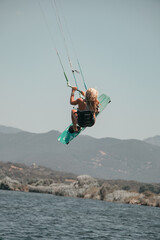 Female kitesurfer in full jump performing an artistic and extreme figure with her board above the water of the Mediterranean Sea in Corsica near Propriano 