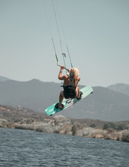 Female kitesurfer in full jump performing an artistic and extreme figure with her board above the water of the Mediterranean Sea in Corsica near Propriano 
