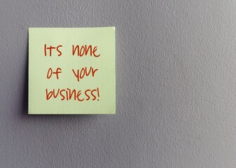 Paper note pad stick on gray wall written IT'S NONE OF YOUR BUSINESS , to tell someone not to get...