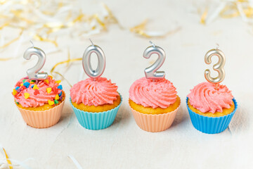 Food concept of New year 2023. Festive cupcakes and candles in form of numbers 2023 on white background.